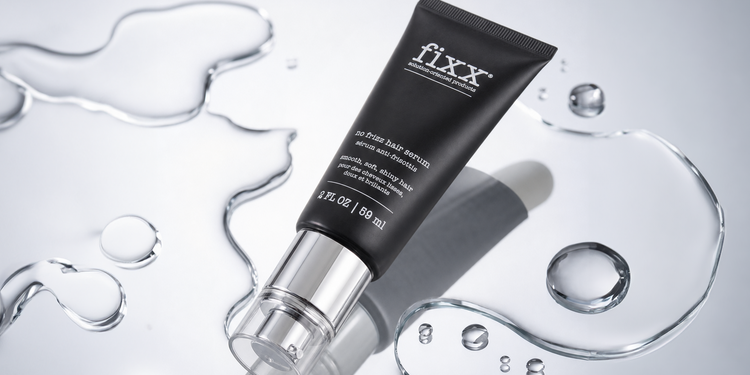A black squeeze tube of fixx skin care product with a clear cap, styled on a reflective silver surface with decorative water droplets and liquid swirls.
