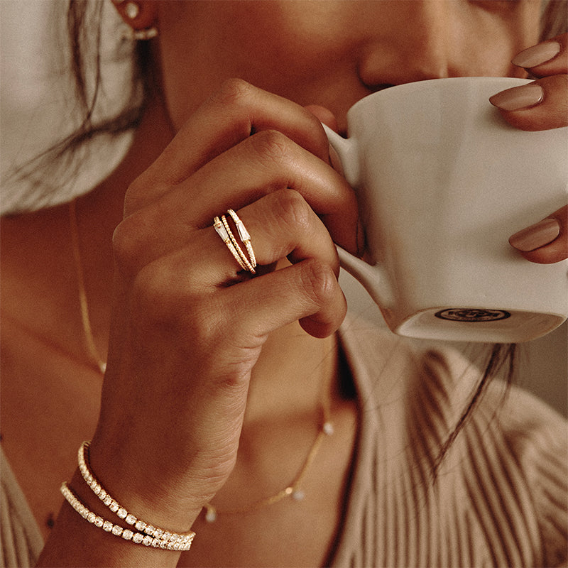 Model wearing Layered Adrienne - Spiraled Baguette Rings, stacked, with clear stones in silver, with other Layered bracelets, drinking coffee