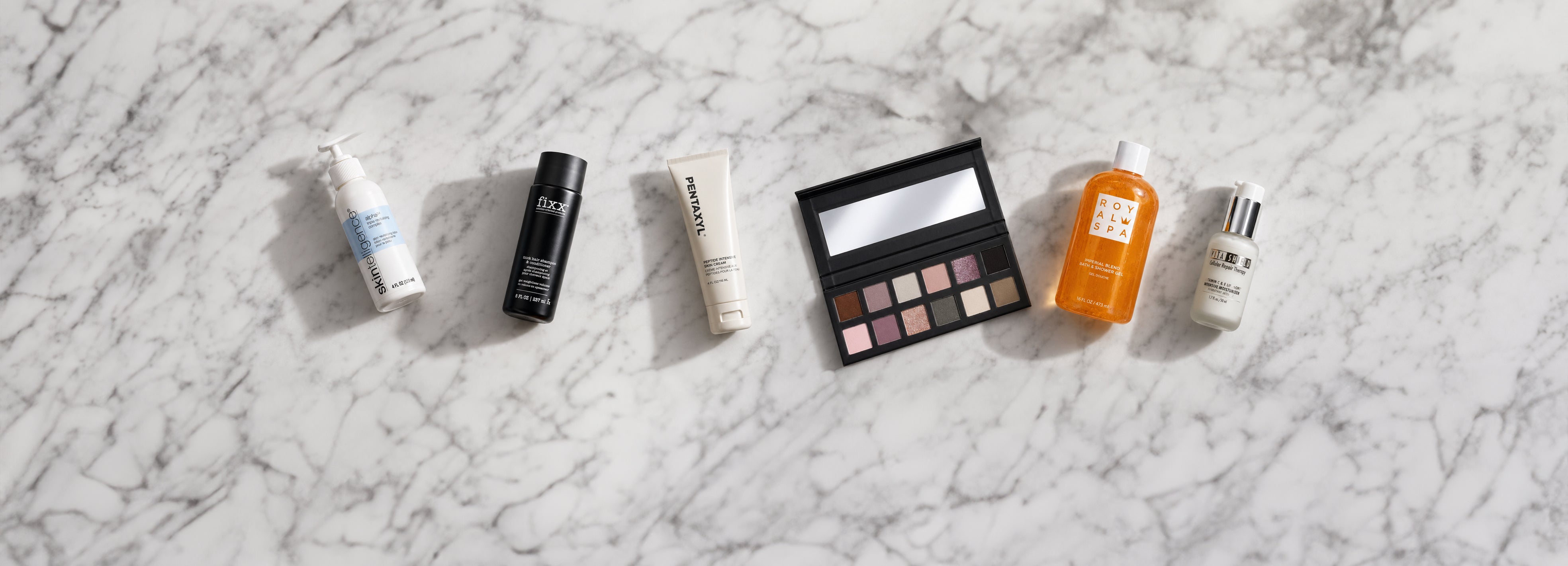 Set of makeup products including bottles and a palette on a marble surface