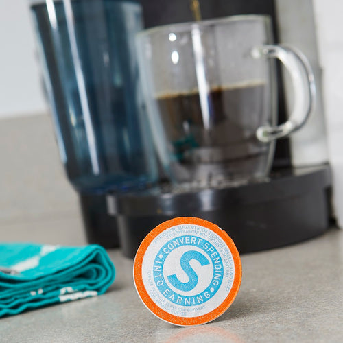 Shopping Annuity Brand Premium Coffee, pod shown with coffee maker and tea towel