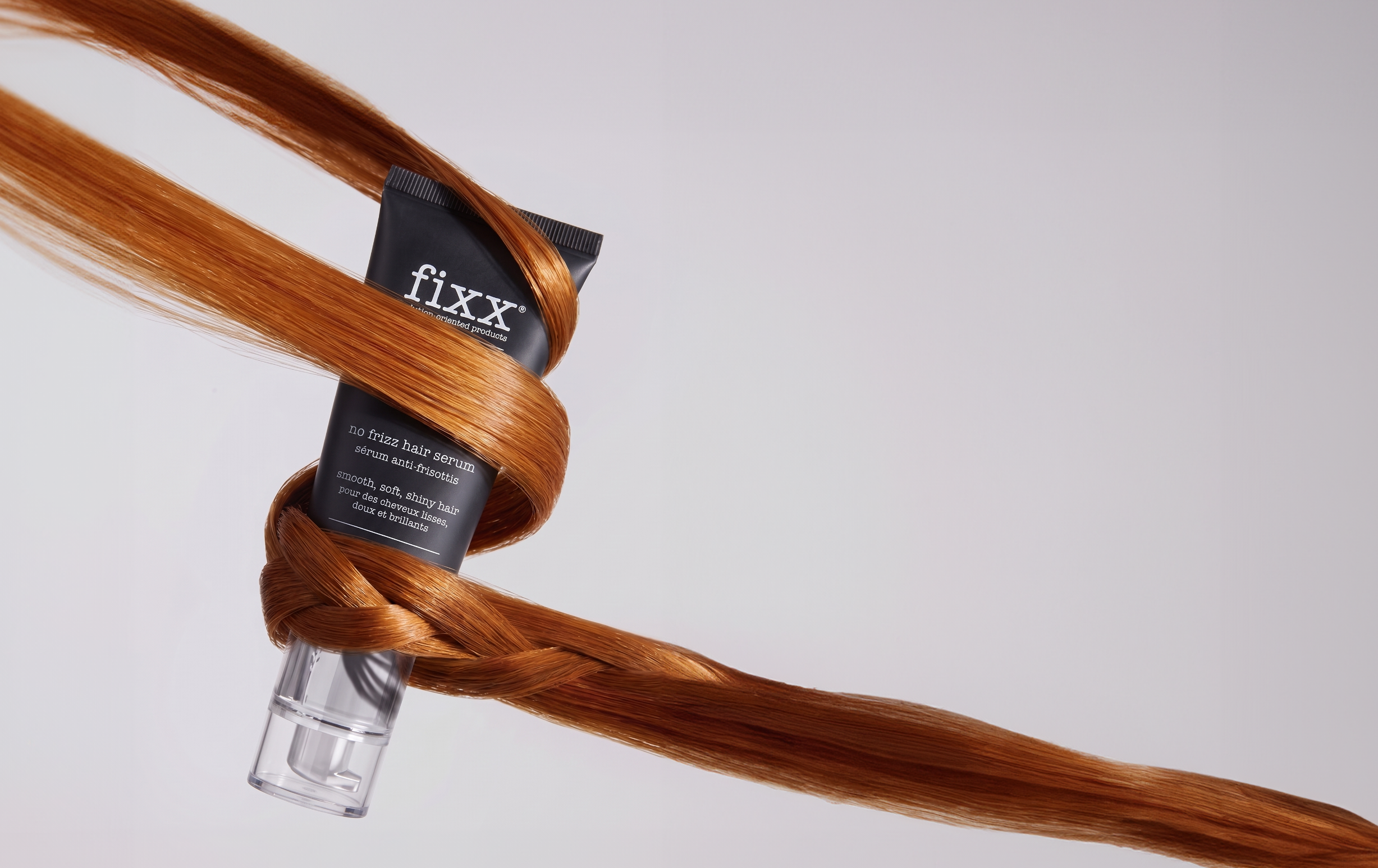 A tube of fiXX hair color wrapped in long, glossy coppery auburn hair against a clean light gray background.