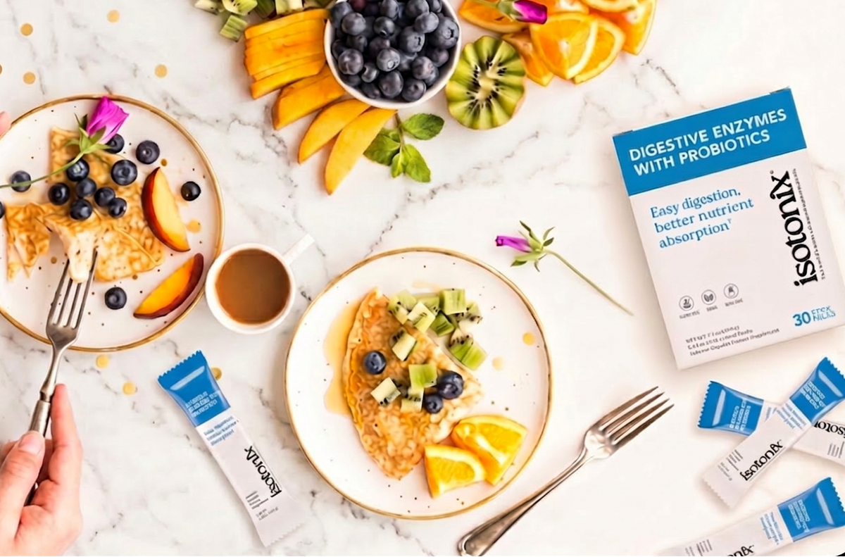An overhead styled breakfast scene on a white marble surface showing two plates of pancakes with fruit, blueberries, kiwi, and orange slices, along with a box and individual packets of Xtendi Digestive Enzymes with Probiotics.