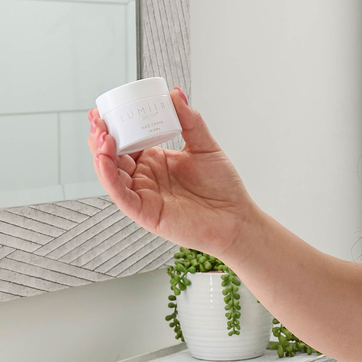 Image of a woman holding a canister of Lumiere de Vie NAD Creme