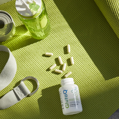 Opened bottle of GutaQ with veggie capsules spilled out on a yoga mat.