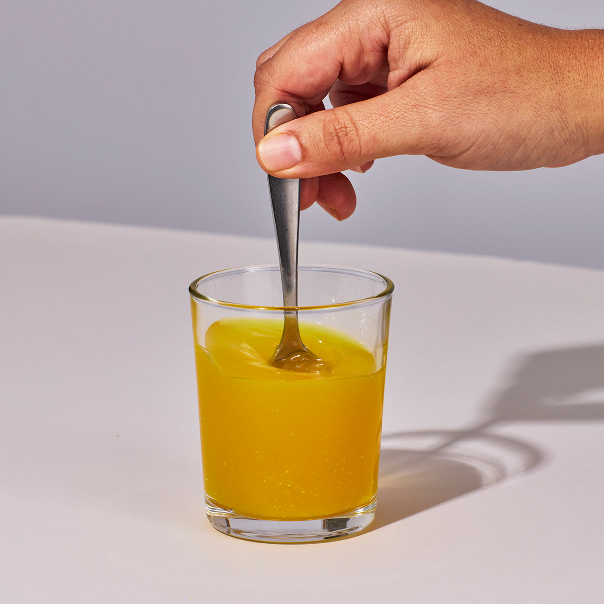 Image of someone's hand mixing up a serving of Isotonix Multivitamin Fifty Plus powder with water.