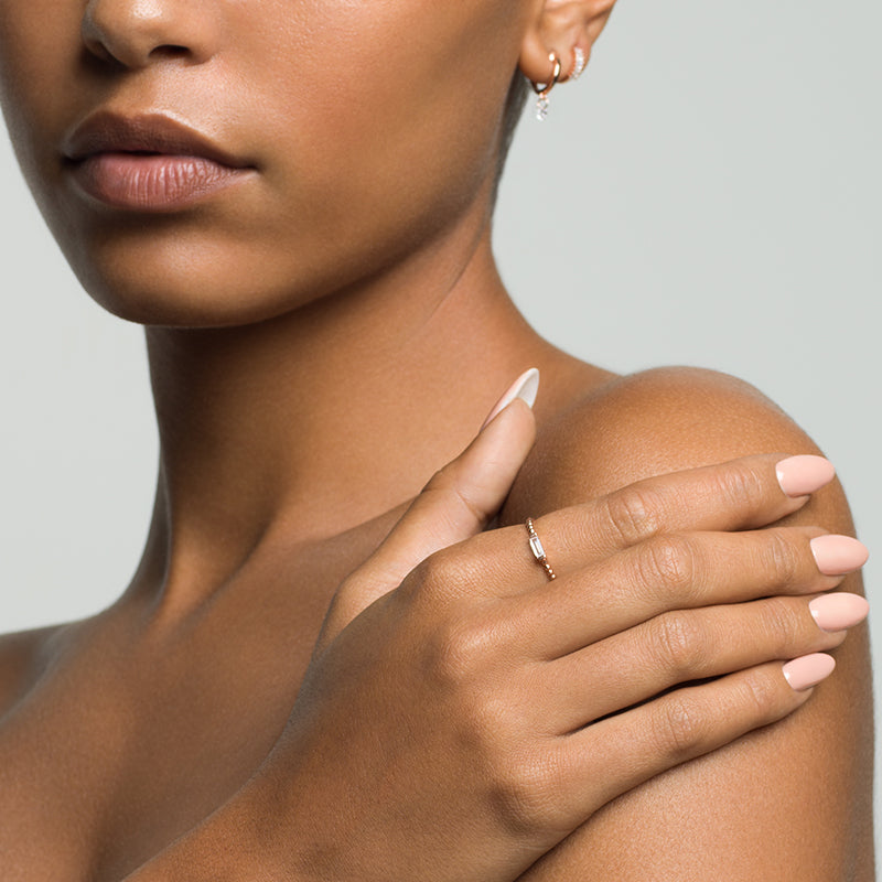 Model wearing Layered Vanessa - Pierced Round Cut Huggie Earrings & Adrienne - Spiraled Baguette Ring, in gold, her hand on her shoulder