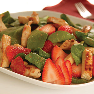 A close-up of a fresh salad in a white bowl, featuring green spinach leaves, sliced red strawberries, snap peas, and grilled chicken pieces.