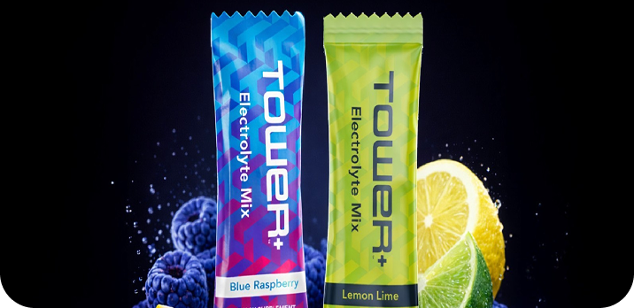 Two Tower Electrolyte Mix packets, one blue raspberry and one lemon lime, with corresponding fruit images on a black background.