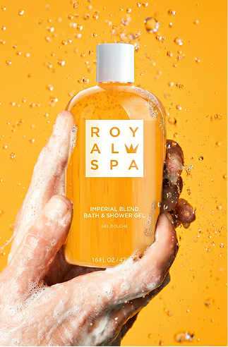 Hand holding a bottle of Royal Spa Imperial Blend Bath & Shower Gel against a yellow background