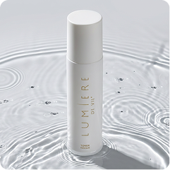 A white cylindrical cosmetic bottle labeled 'LUMIÈRE Paris' stands upright in a water ripple effect on a light gray background.