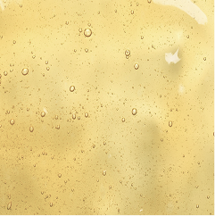 A close-up of a pale golden yellow liquid or gel with small scattered droplets and a soft mottled texture.