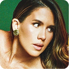 A close-up portrait of a woman with brown hair wearing a textured gold earring, set against a solid green background.