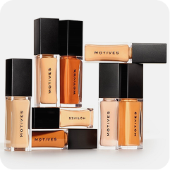 A group of MOTORS brand liquid foundation bottles and matching rectangular boxes, arranged together on a light gray background. The bottles contain shades of beige, tan, and orange-brown liquid, and the packaging features black caps and gold lettering.