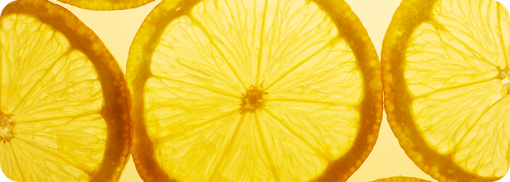 Close-up of bright yellow lemon slices with visible pulp and rind against a pale yellow background.