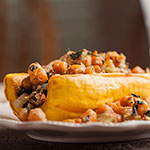 A close-up of a plated food dish, likely stuffed yellow rolls or omelet-like wraps filled with a chunky orange and brown mixture, served on a white plate against a blurred warm brown background.