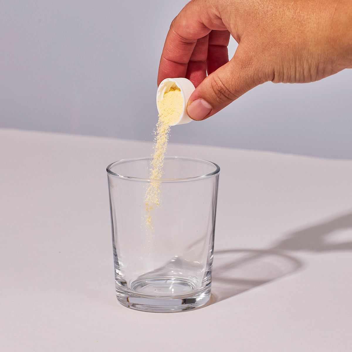 Image of someone's hand pouring a serving of Isotonix Multivitamin Fifty Plus powder into a glass.