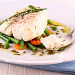 A plated dish of white fish with green beans, carrots, and a drizzle of oil on a white plate.
