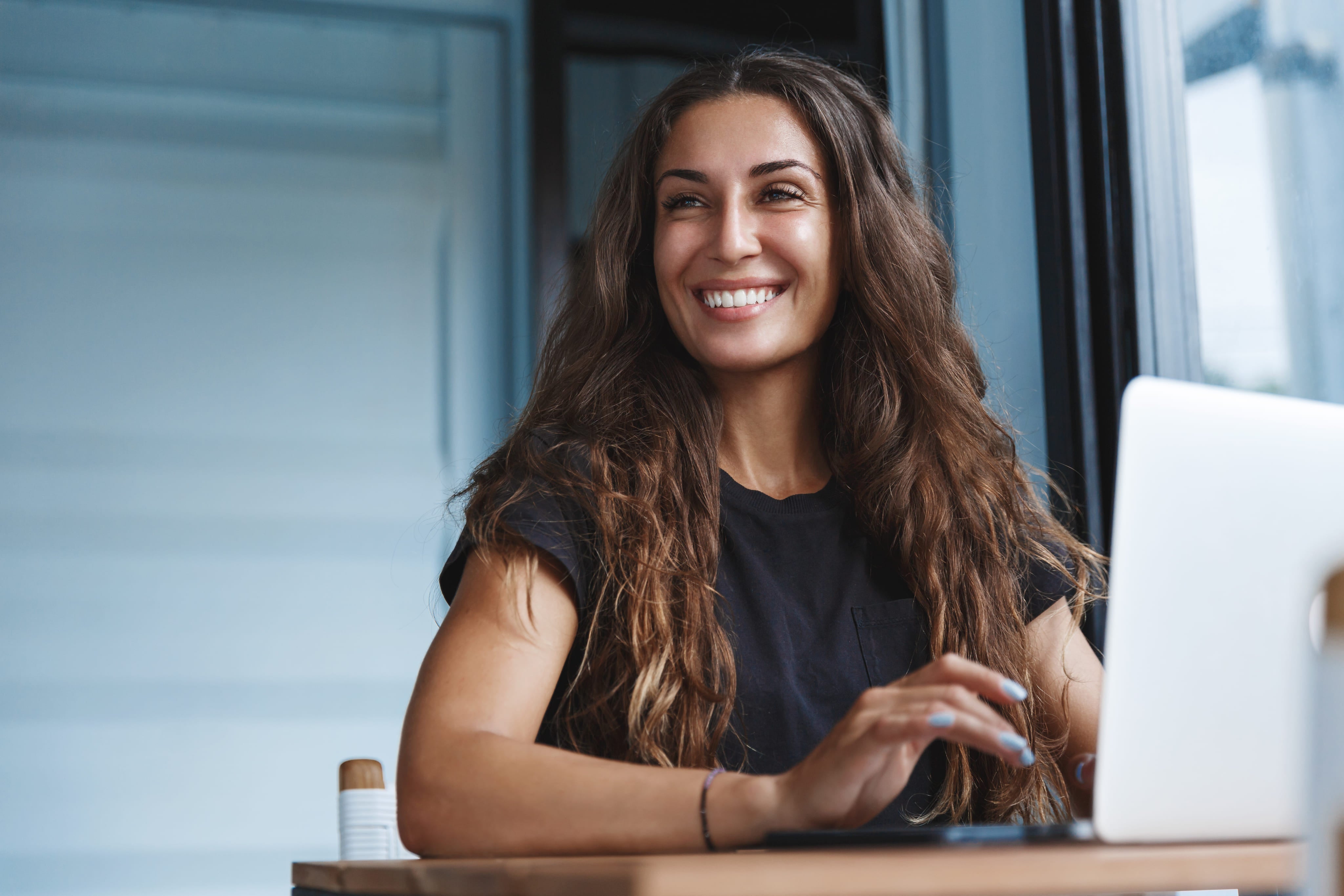 Woman sitting at a table with a laptop, smiling.