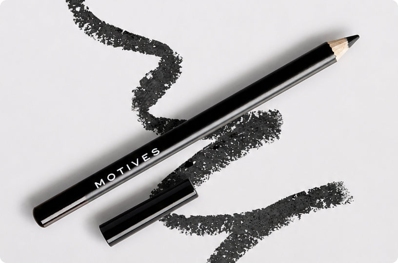 A black cosmetic eyeliner pencil with the brand name 'MOTIVES' printed in white on the barrel, shown with its cap removed and placed beside it on a white background with black makeup swatches.