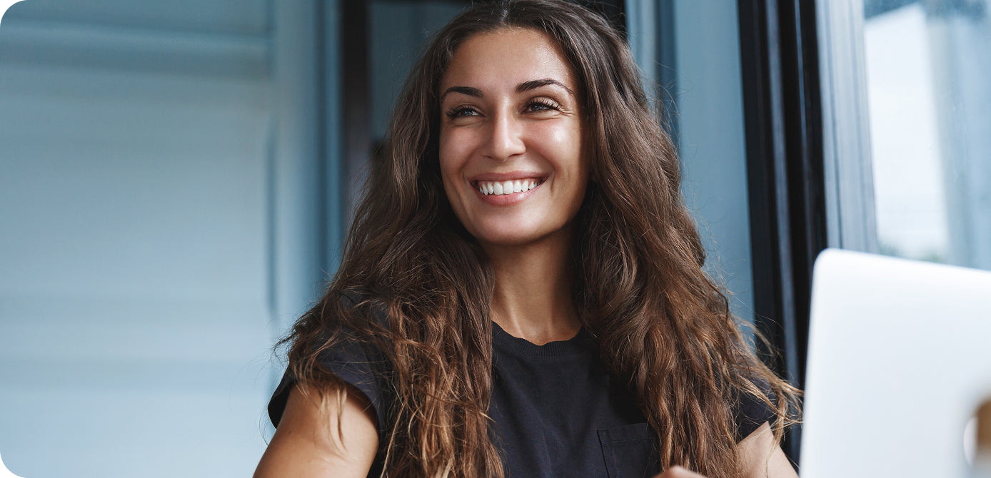Woman with long brown hair smiling in front of a laptop.