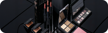 Makeup products including lipsticks and palettes on a black surface
