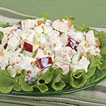 A close-up of a creamy chicken salad with red onion and celery on a bed of green lettuce, served on a green plate against a green striped background.