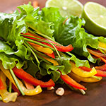 A close-up of a fresh salad with green lettuce, red and yellow bell pepper strips, and lime wedges on a dark plate.