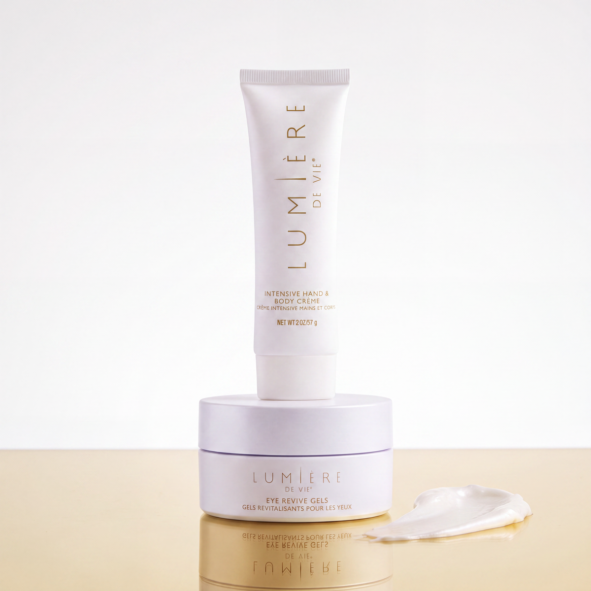 Lumère De Vie Intensive Hand & Body Cream in a white squeeze tube, displayed on top of a matching white jar with a smear of cream on a reflective gold surface against a white background.