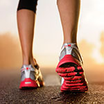 A close-up shot of a person's feet wearing red, white, and gray running shoes on an asphalt road with a warm, blurred background.