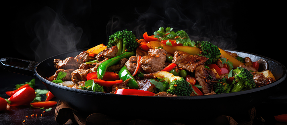 A black cast-iron skillet filled with a colorful stir-fry vegetable and meat dish, photographed on a dark background with steam rising from the food.