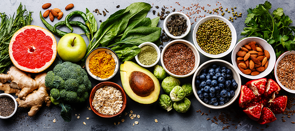 Assorted healthy foods including fruits, vegetables, and grains on a gray surface