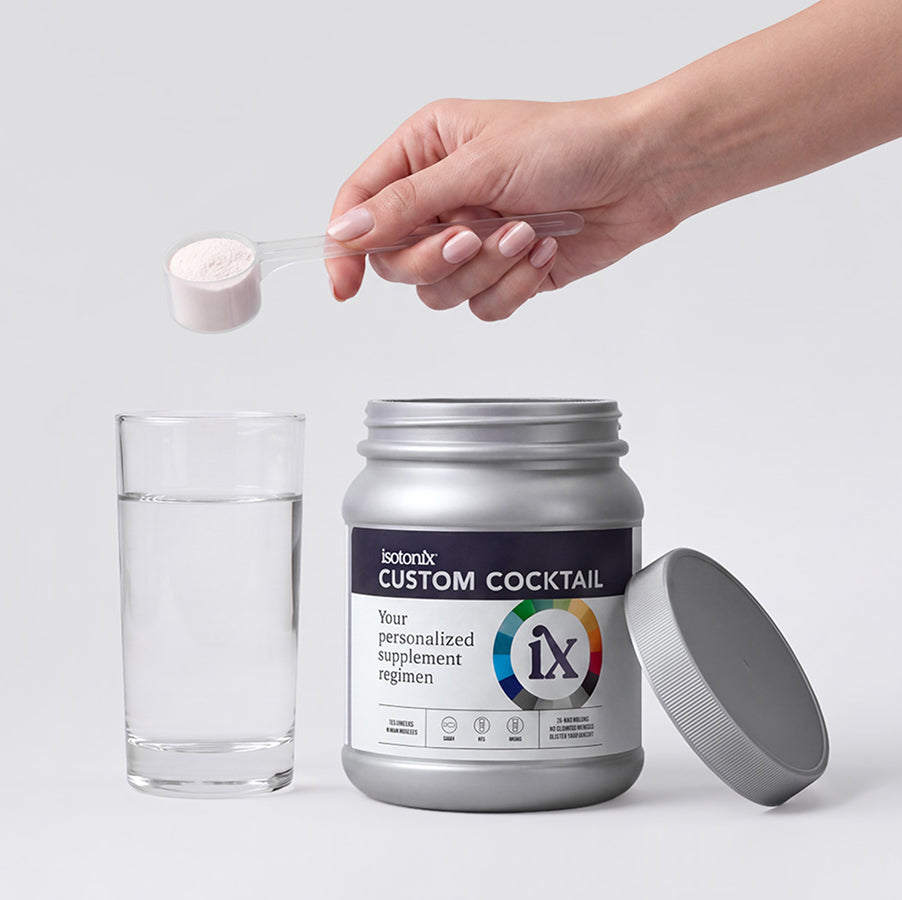 A hand holds a small clear scoop filled with pale pink powder above a glass of clear liquid and a silver supplement jar labeled 'bolonyx CUSTOM COCKTAIL' with the lid beside it, on a light gray background.
