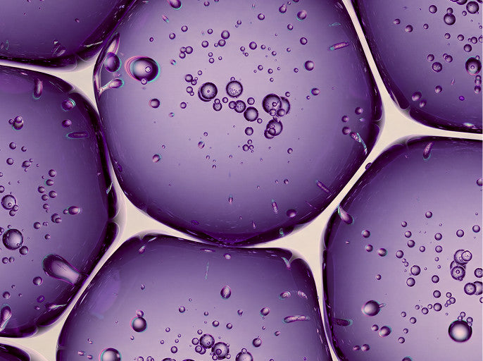 Purple translucent gel beads with water droplets, arranged in a close-up pattern against a light beige background.