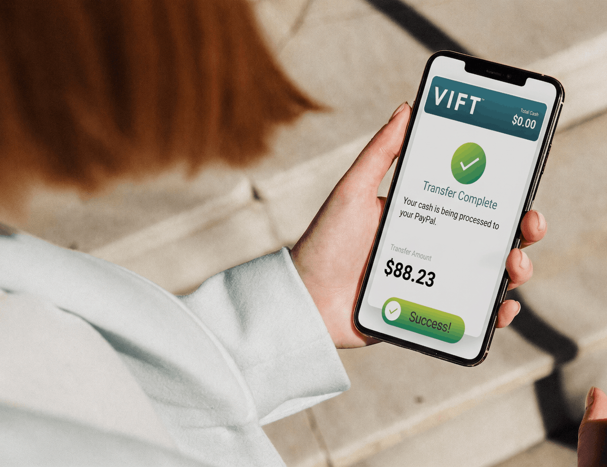 A person in a white jacket holds a smartphone showing a VIFT payment transfer screen with a green checkmark and the text 'Transfer Complete' and '$88.23' against a blurred outdoor background.